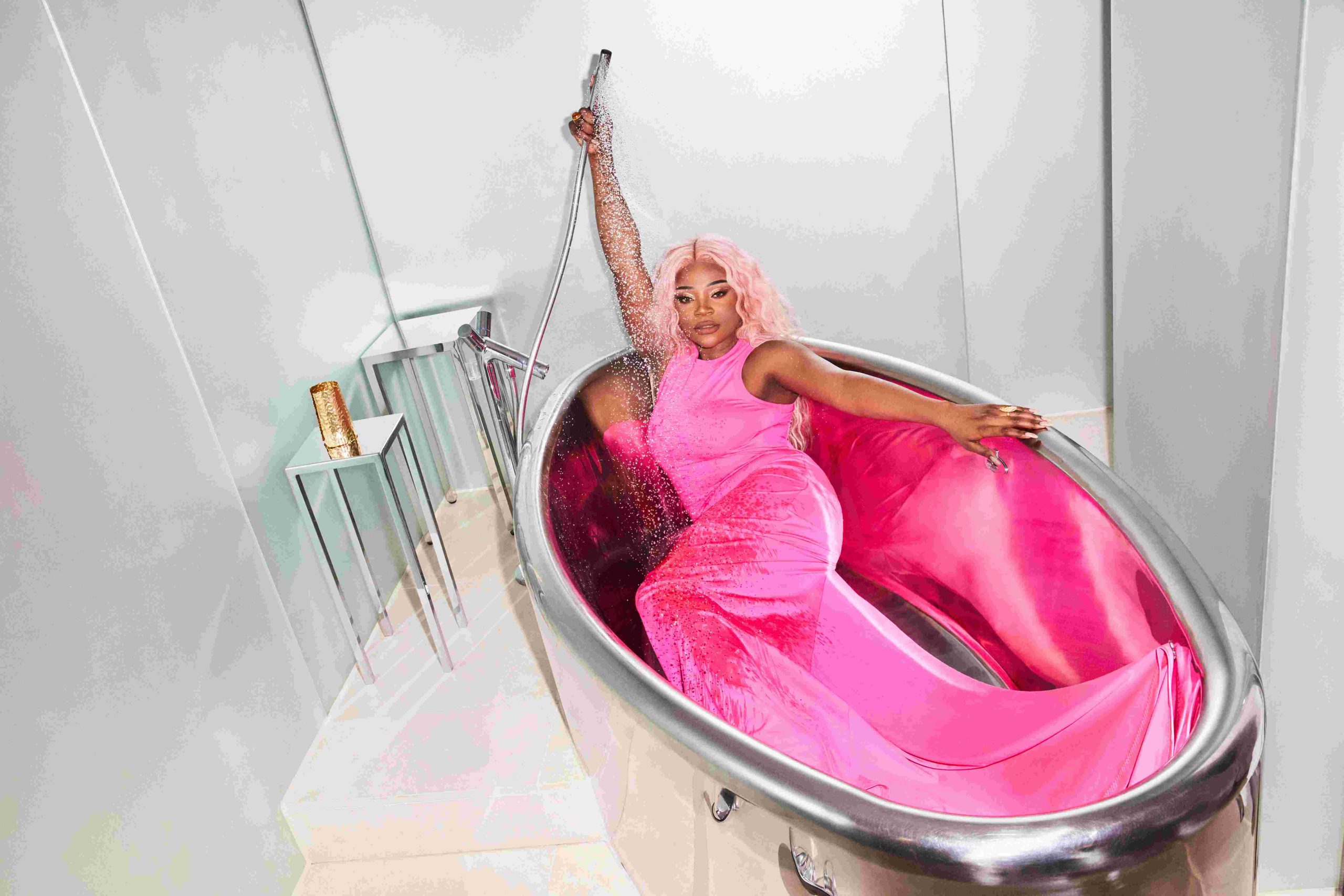 Juliette Fox in pink dress laying in silver bath tub spraying water on herself at Sanderson London