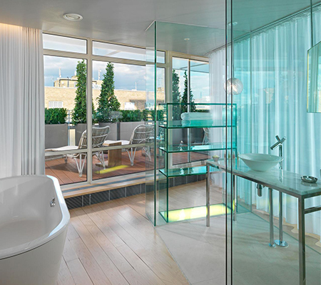 Bathtub with curtains and glass doors overlooking a terrace with large green plants