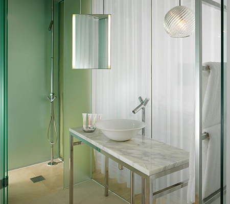 Marble bathroom sink with overhead pendant lighting and standing shower with green wall