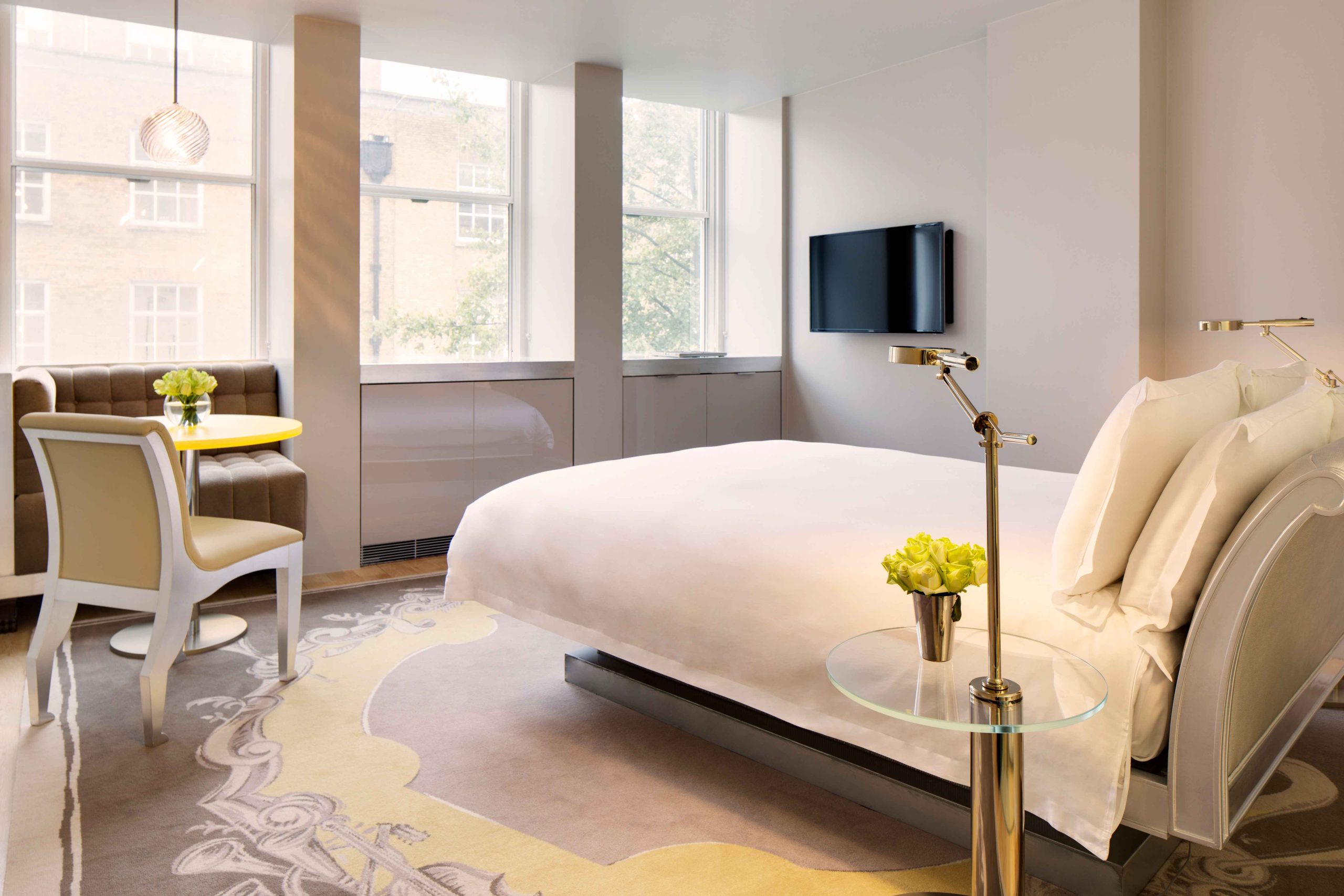 White bed, tv on wal, banquet seating, chair, and windows in a room at Sanderson London