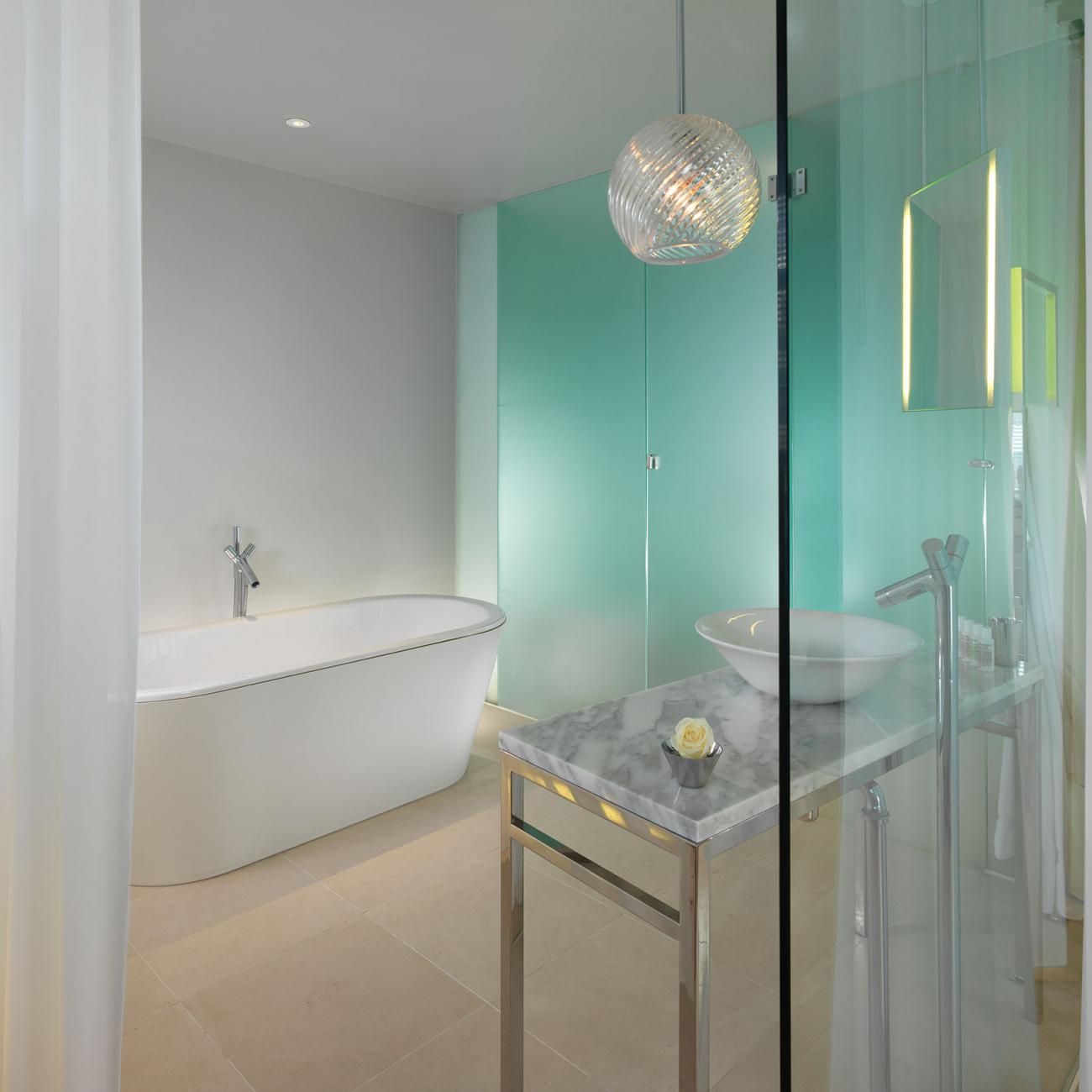 Bathroom with large white bathtub, turquoise wall, marble sink, and glass walls