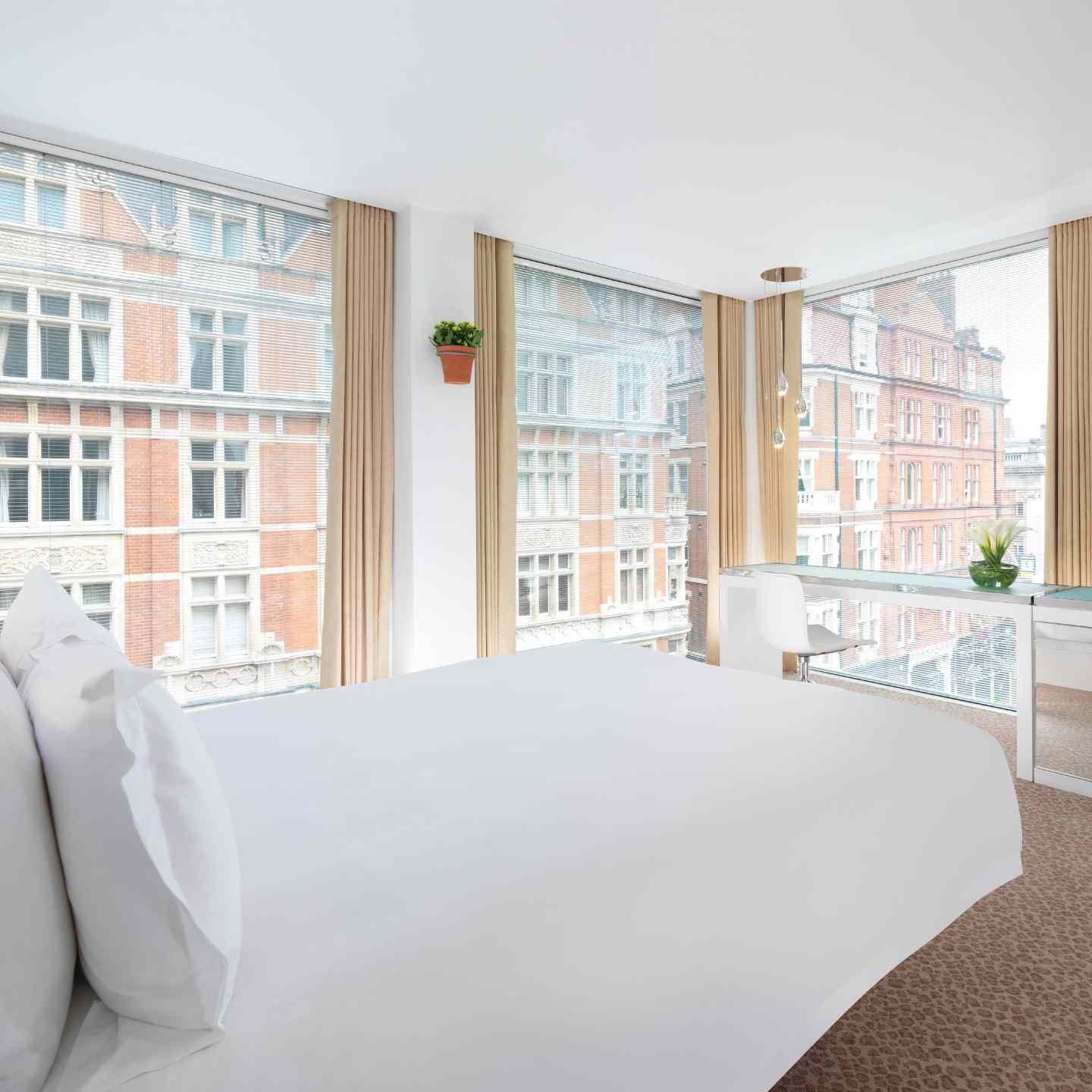 White bed angled with large windows on all corners looking out to London buildings in a St Martins Lane room