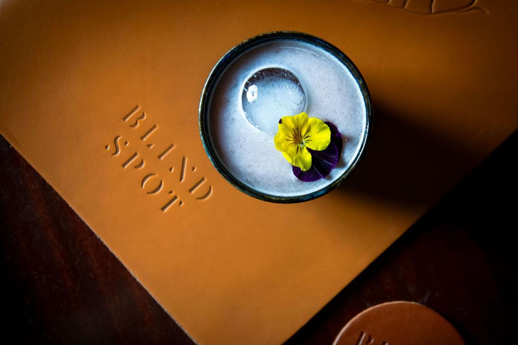 Brown branded 'Blind Spot' coaster with a dish with flower in it. 