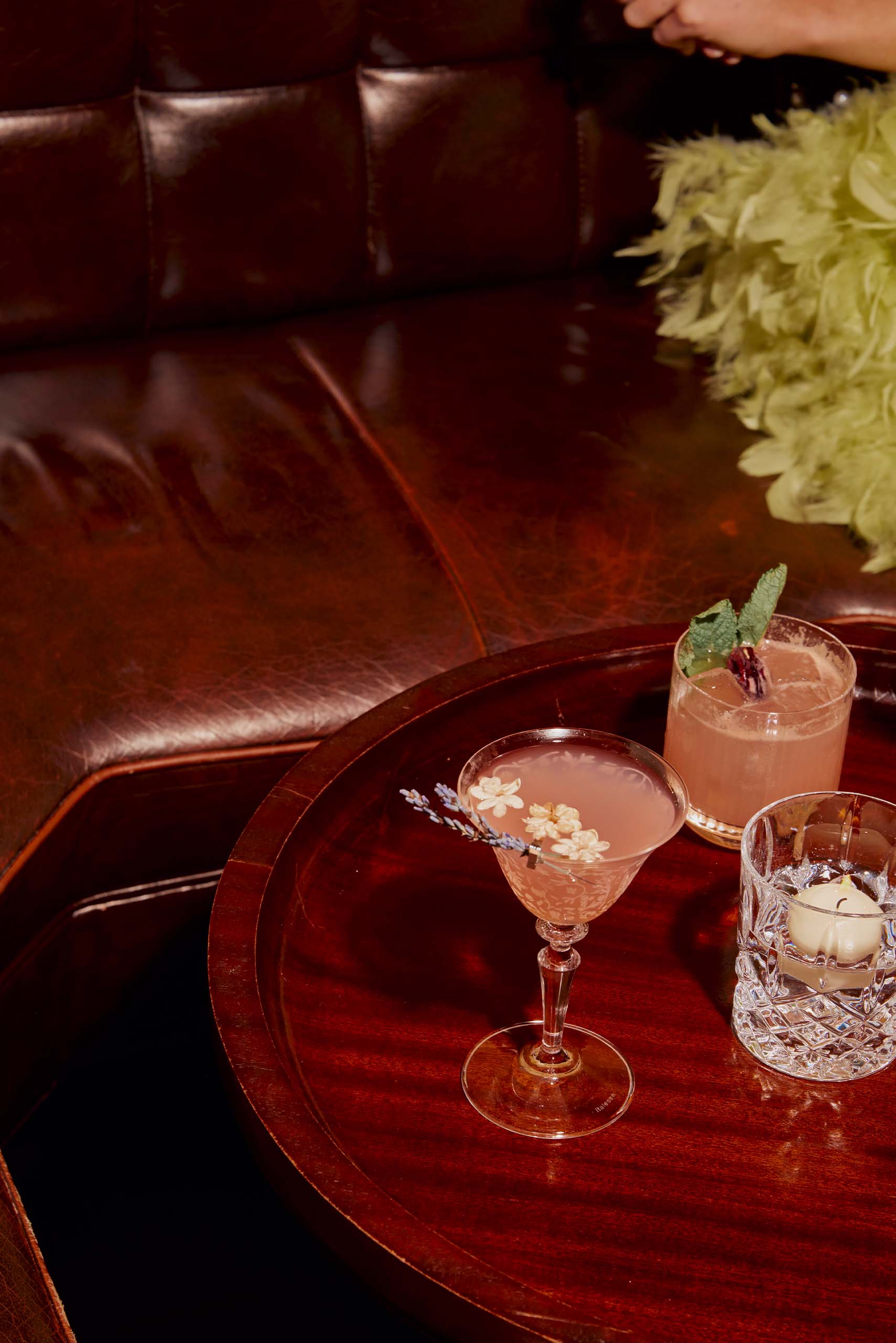 two pink cocktails sitting on a rosewood table.