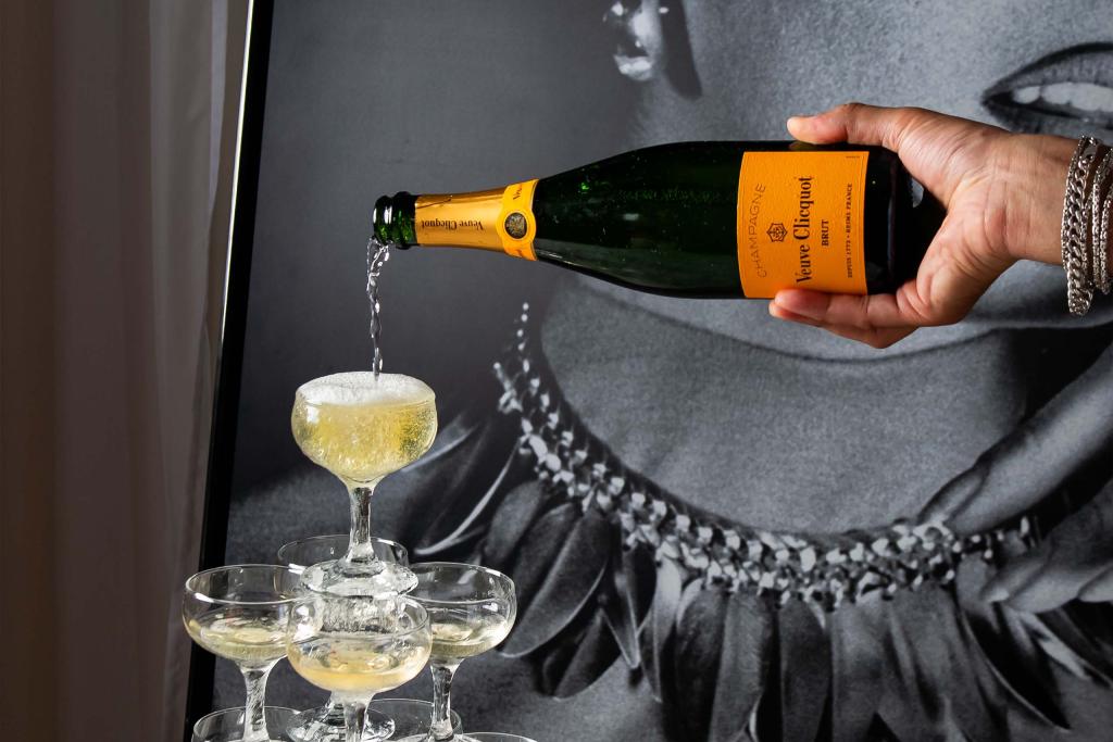 Hand pouring champagne into the top glass and let it cascade down to fill the underlying glasses.