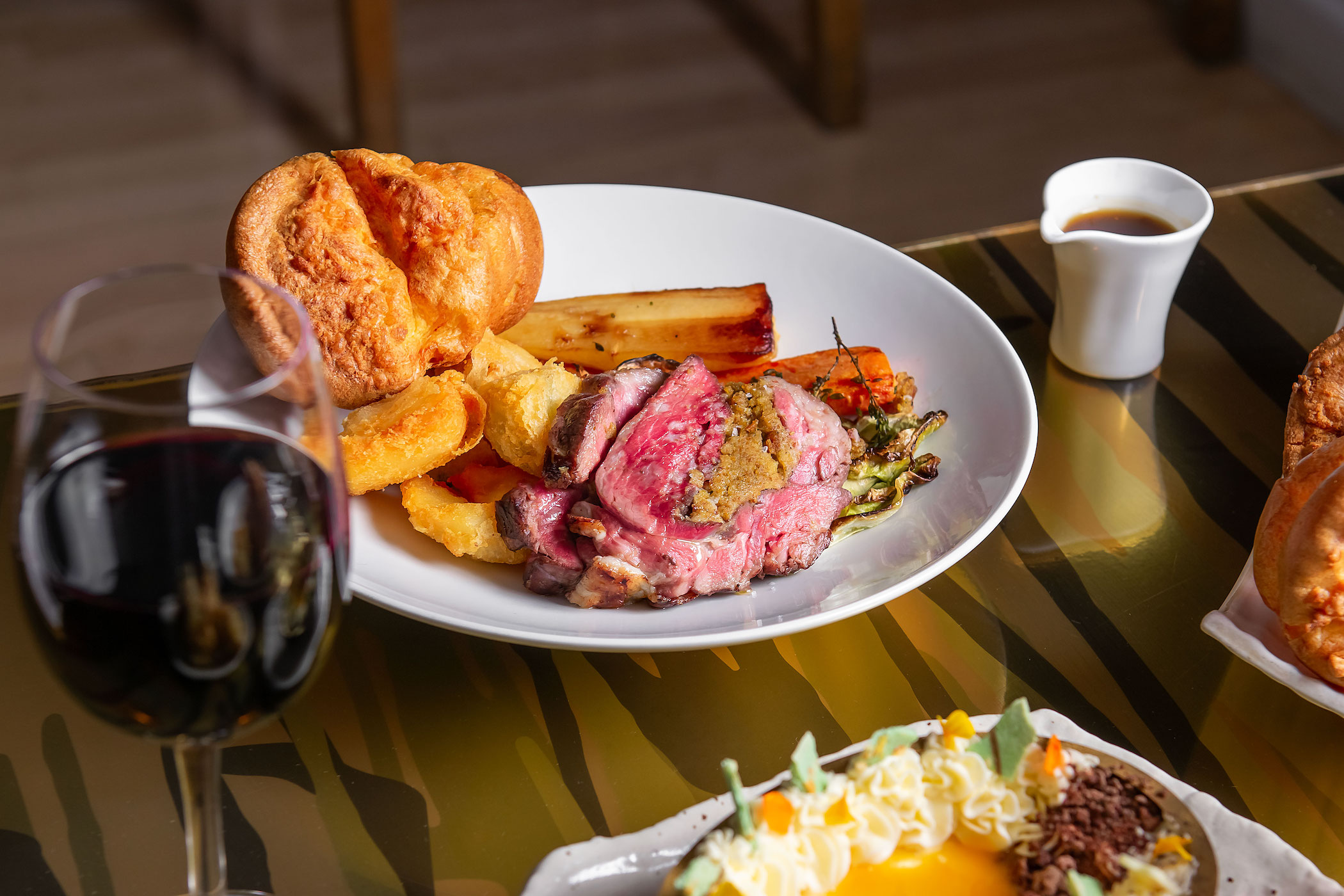 Roast with a popover and vegetables on a round white plate with a glass of red wine on a wooden table