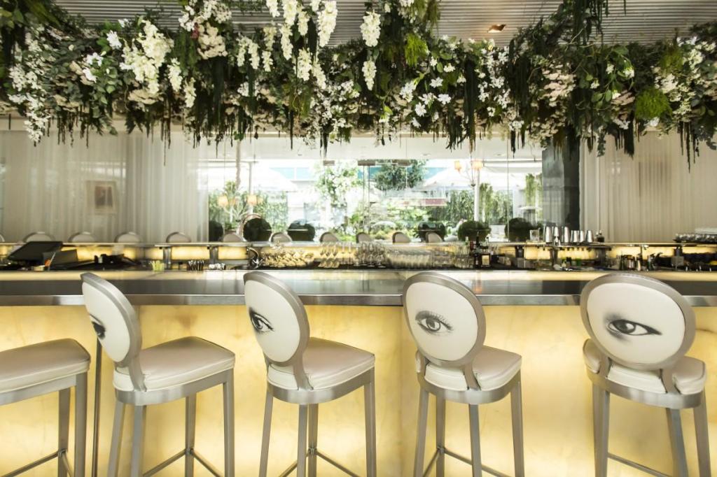 Silver bar with floral arrangements at the top and four barstools all with eyes printed on the back of them