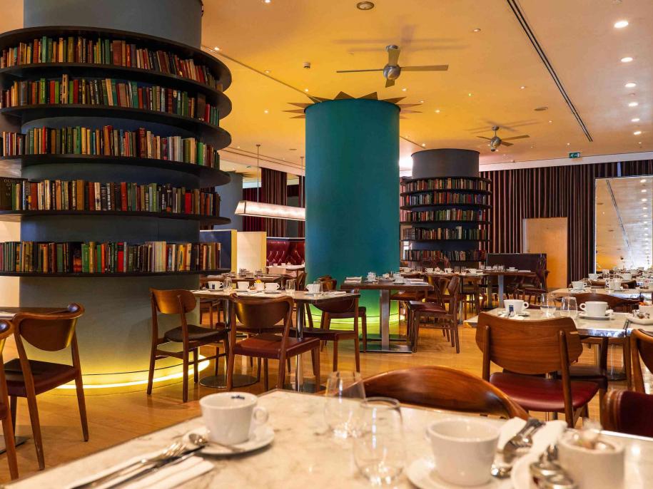 Restaurant dining room with circular bookshelves, large turquiose bannister, and marble tables with wooden chairs