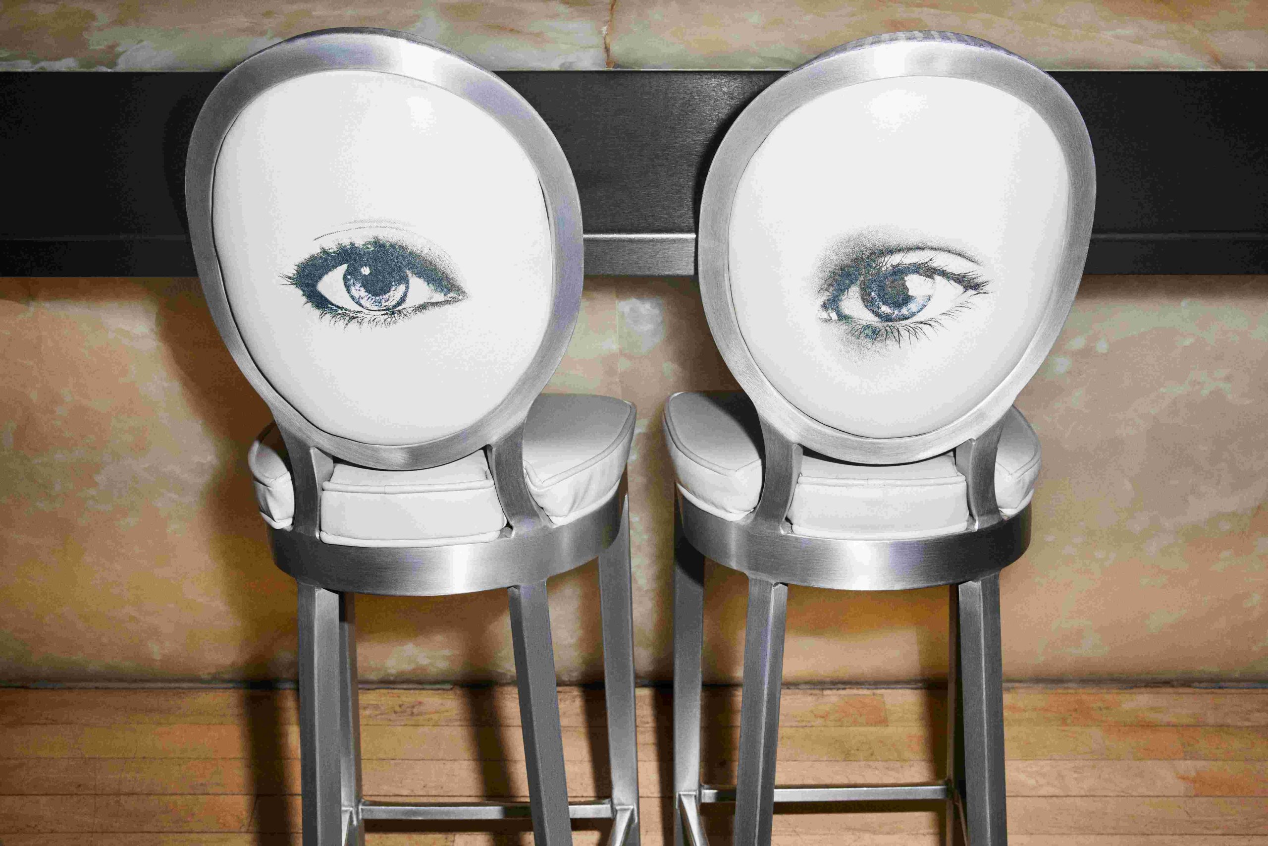 Two barstools with eye printed background pushed up to a silver bar