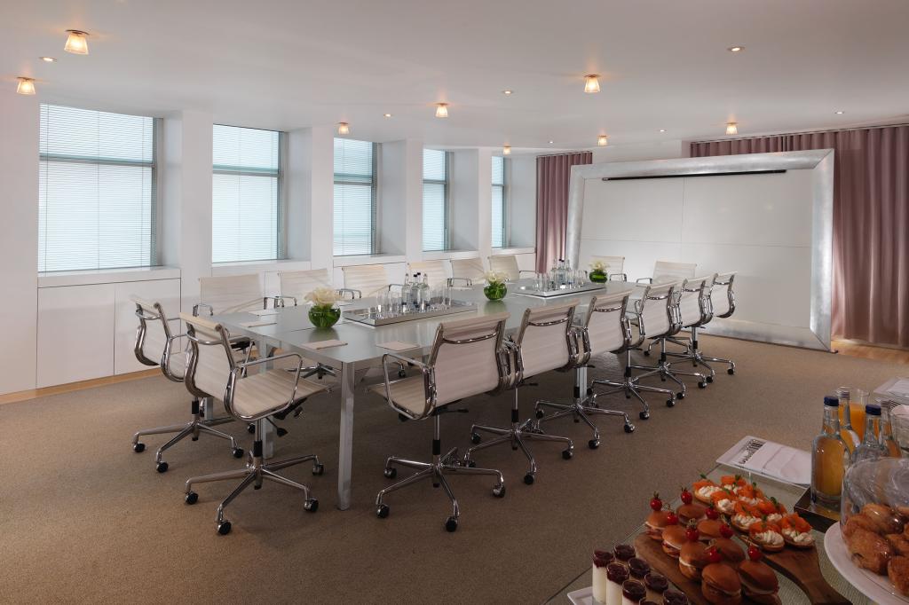 Large room with big rectangular table with floral arrangements on top and white desk chairs surrounding it