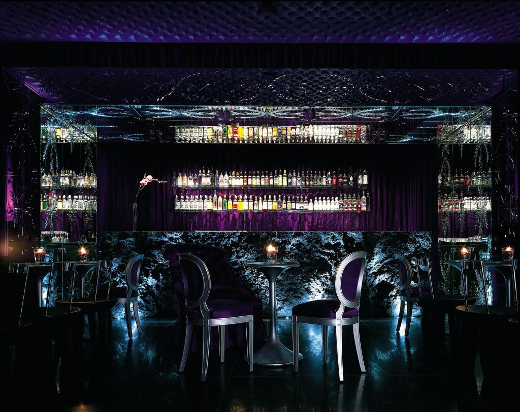 Purple bar with liquor bottles in the background and small round tables and chairs in foreground