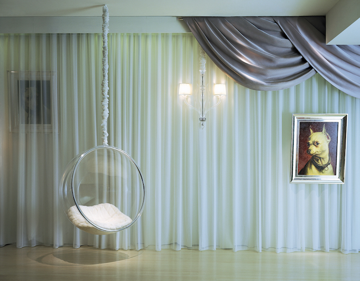 Lobby with white curtains, hanging clear bubble chair, and portrait of a small white dog on the wall