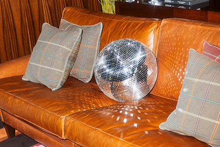 Light brown leather sofa with grey plaid pillows and shiny disco ball