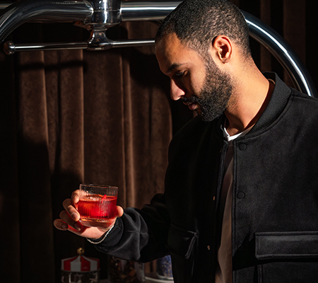 Man in black shirt with beard holds a red cocktail