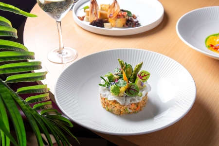 Tartare on a white plate on a light wooden table with other white plates surrounding