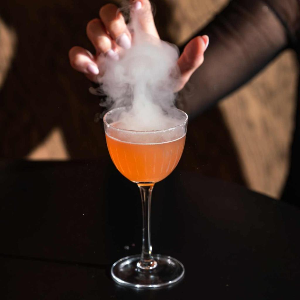 Orange cocktail in glass with smoke rising above it and hand above the smoke