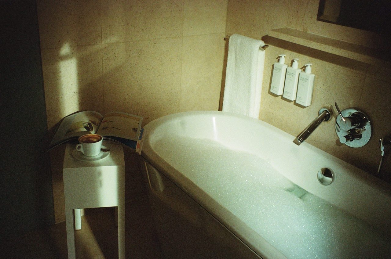 White bathtub with bubbles and white side table with coffee and magazine