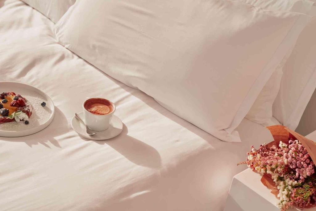 Coffee and breakfast dish on white bed with bouquet of flowers on bedside table at St Martins Lane