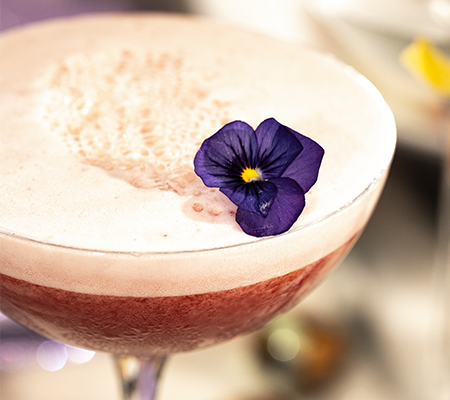 Close up of cocktail garnished with a small purple flower