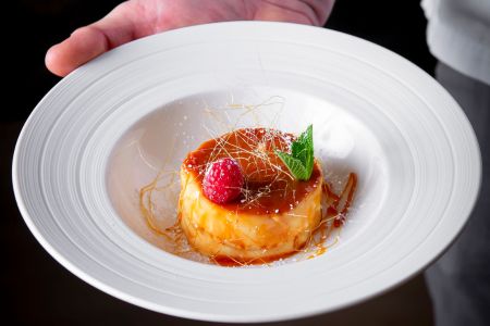 Creme brulee on a white plate being held by a hand