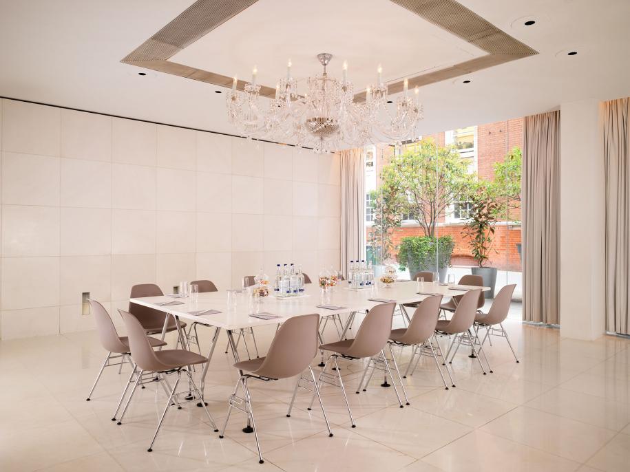 Large white room with glass chandelier and large white table in the middle surrounded by gray chairs