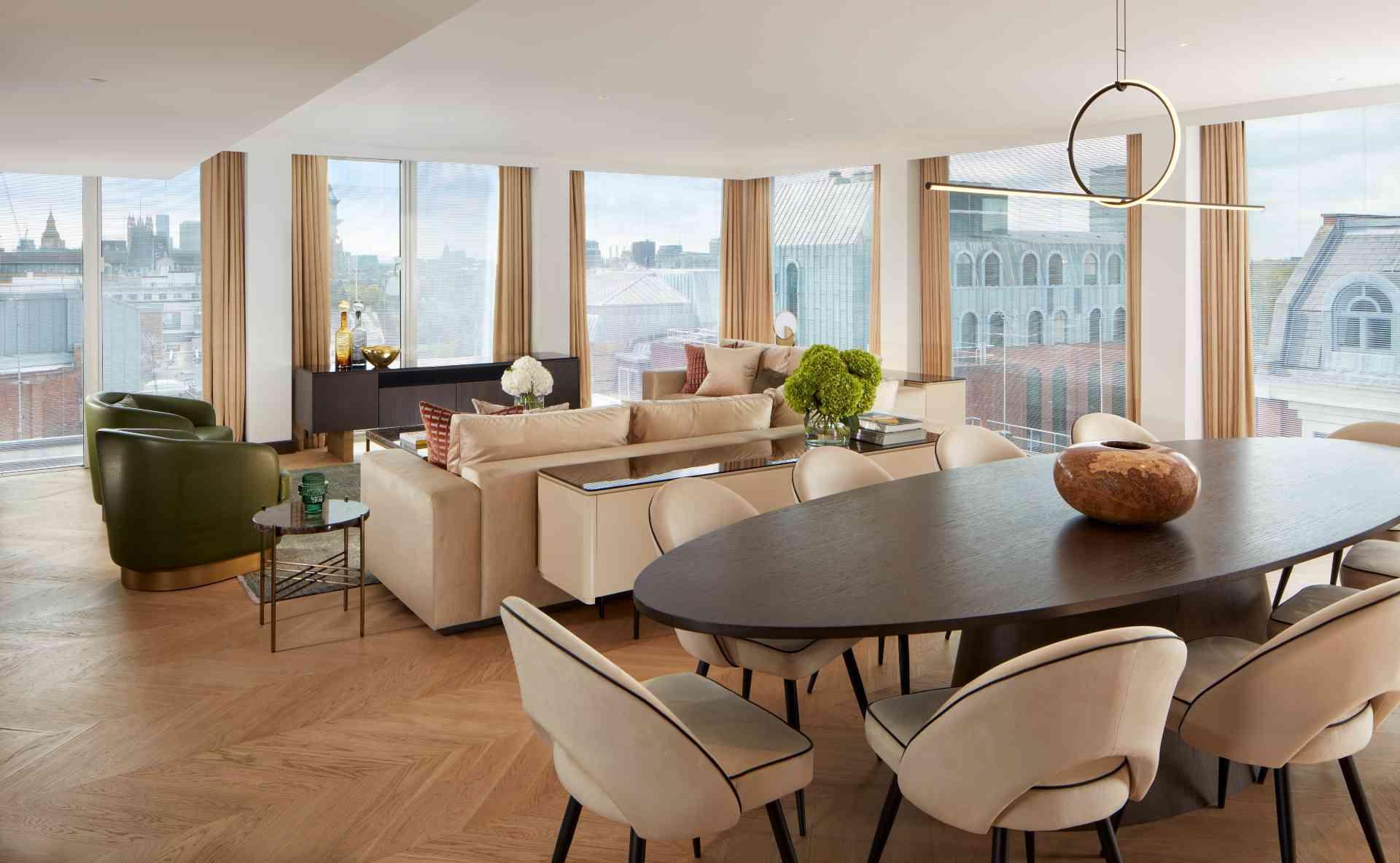 Oval dark brown table with beige suede chairs and beige sofas and green lounge chairs in the background at St Martins Lane Penthouse