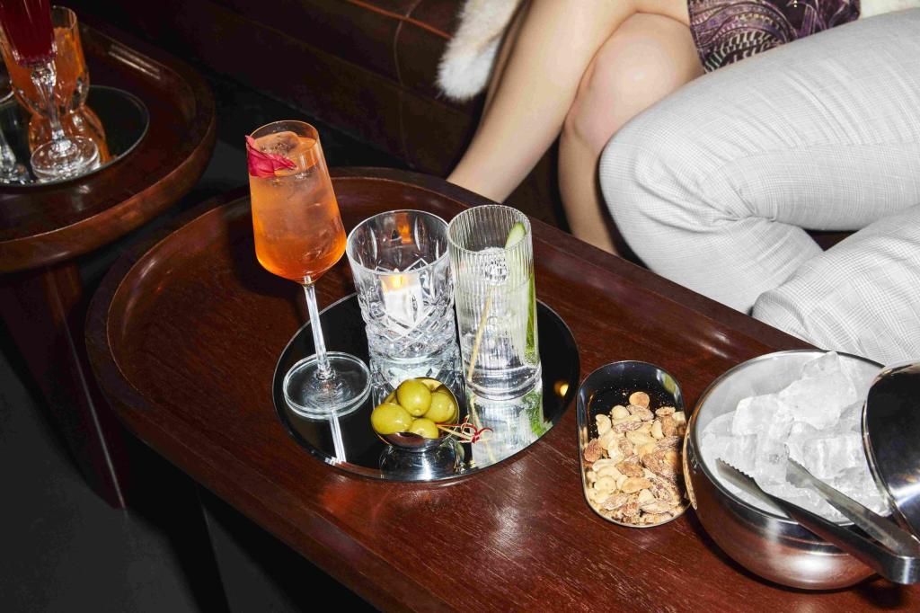 Various cocktails on dark wooden table with olives and snacks at The Den at St Martins Lane