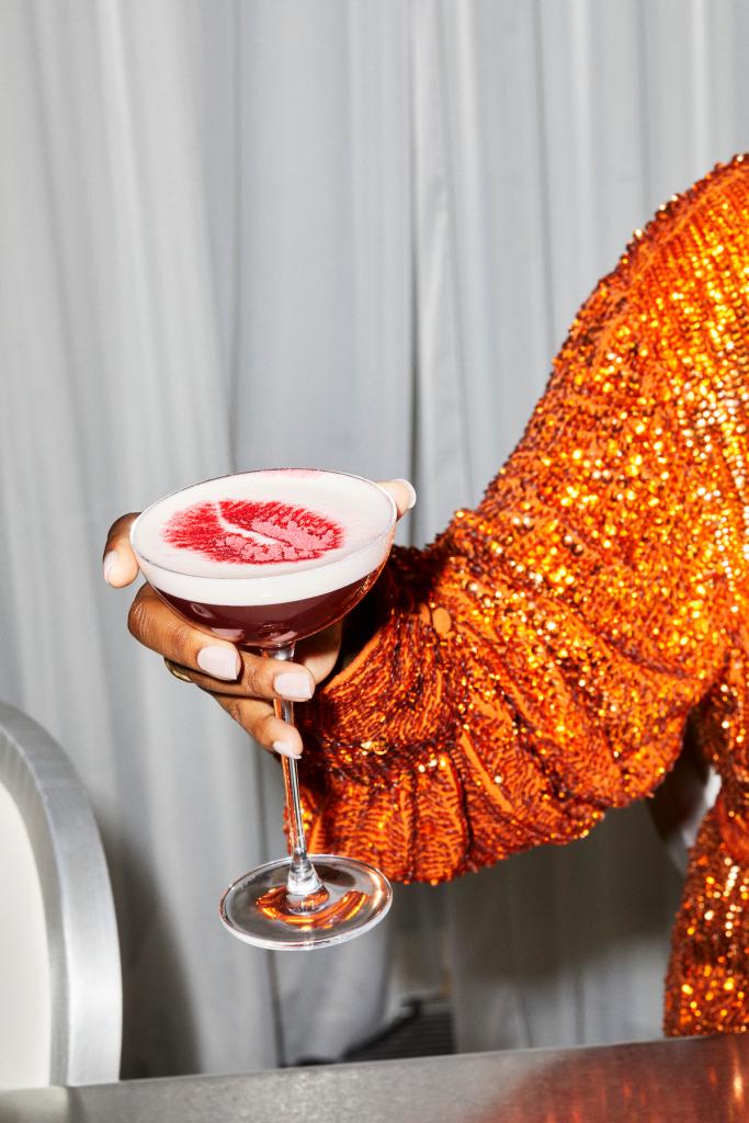 Cocktail with lipstick design being held by a woman in orange glittery blouse