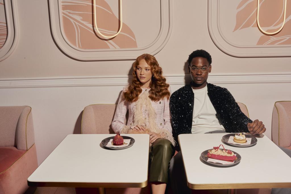 Man and woman sit next to each other on pink booth with table of desserts in front of them