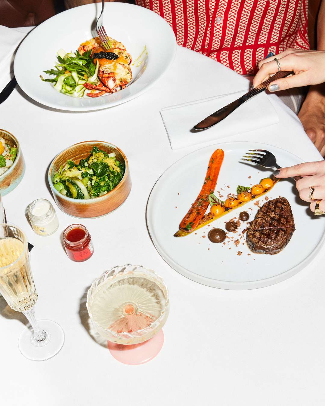 Filete, copas de champán y verduras sobre una mesa blanca en St Martins Lane