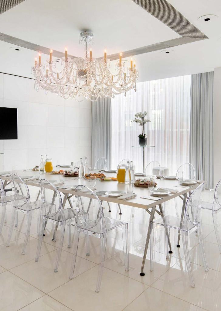 Bright white boardroom with opulent chandelier and large rectangular table with clear chairs