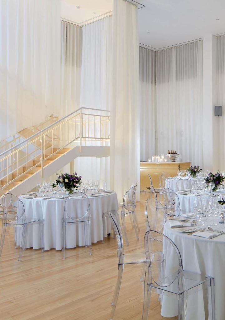 Ballroom with white curtains and large round tables with white tablecloths and clear chairs
