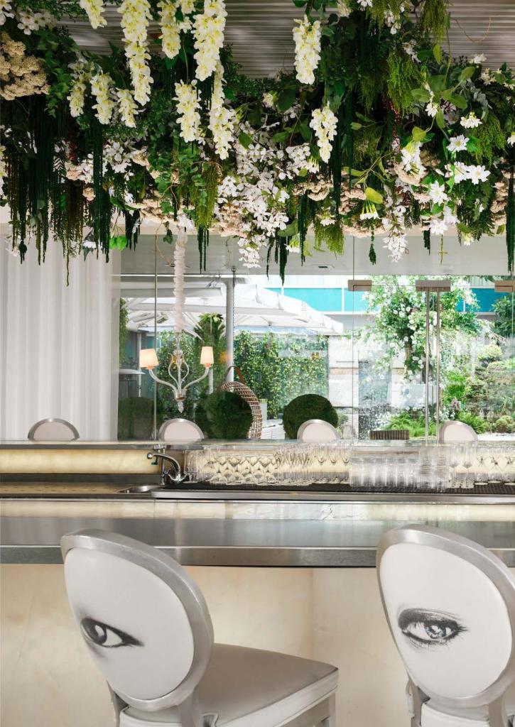 Silver bar with greenery decorations and white bar stools with eyes printed on back