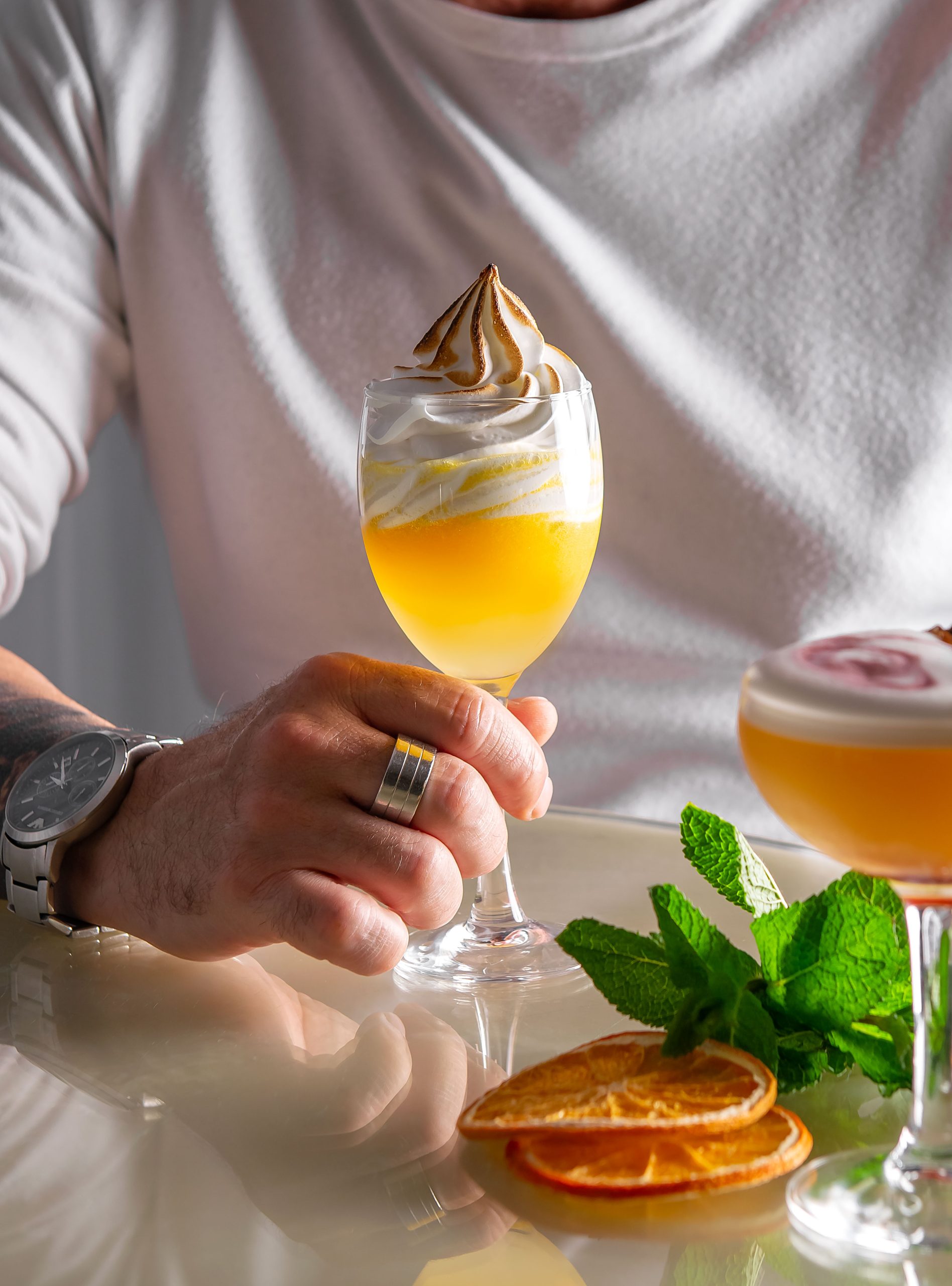 Orange cocktail with whipped topping and man holding the glass with watch and ring