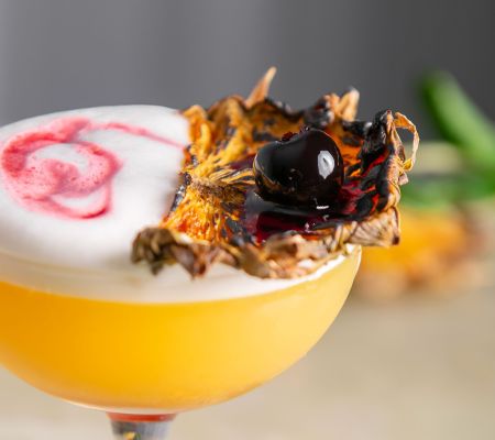 Orange cocktail in a coupe glass with pineapple and blueberry garnish
