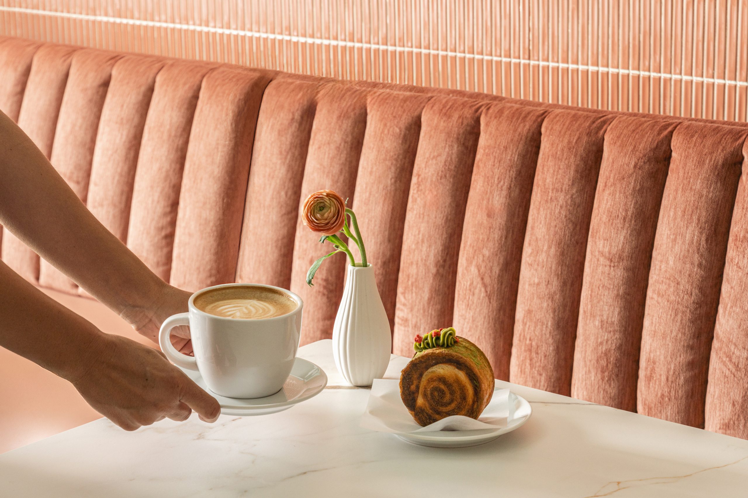 Close-up of a steaming cup of coffee and a flaky croissant on a pink and a white table