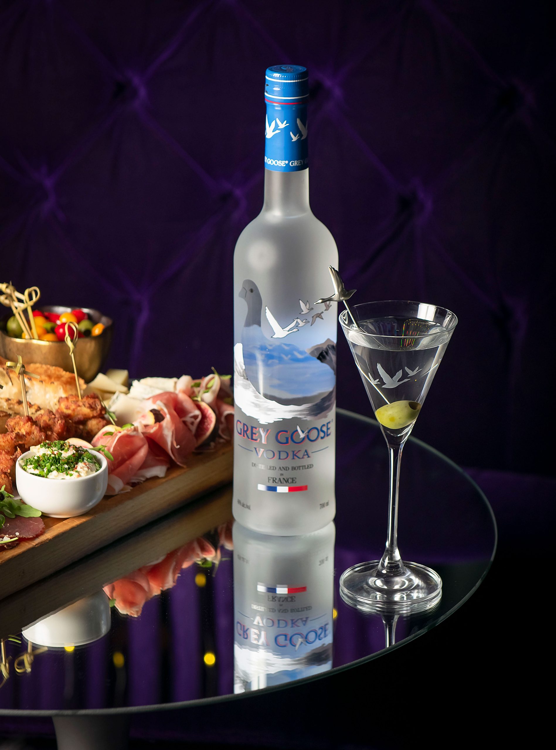 Grey Goose Vodka bottle. Martini with olive inside. Purple Bar.
